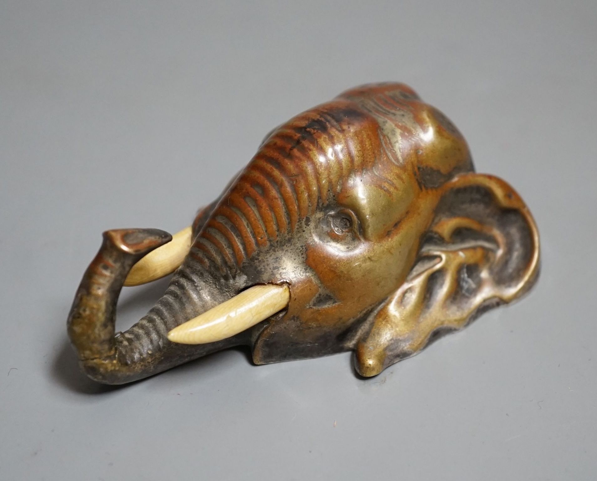 A bronze elephant head paperweight, early 20th century, with ivory inset tusks - 9cm high